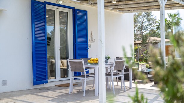 Une terrasse extérieure avec une table et des chaises, une porte bleue à volets et une vue sur les environs.
