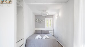 Une petite pièce comprenant un lit, un ventilateur de plafond, un décor mural représentant des poissons et une fenêtre avec des stores.