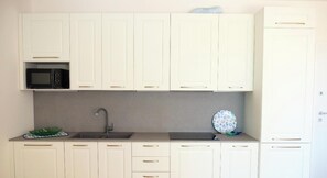Cozinha com armários brancos, micro-ondas preto, pia e um prato decorativo azul.