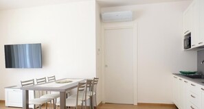 Uma área de refeições com uma mesa e cadeiras, um armário branco com micro-ondas e uma porta com um aparelho de ar condicionado em cima.