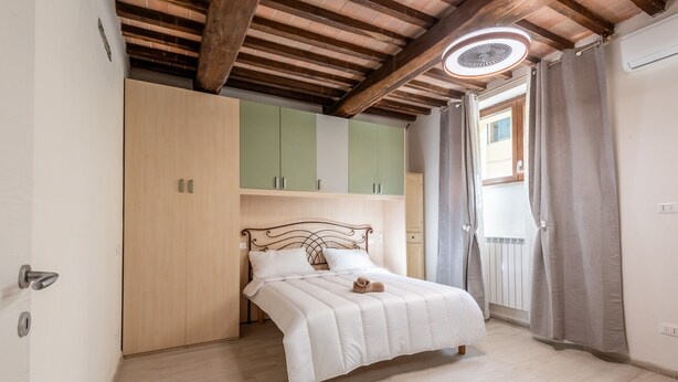 A bedroom with a bed, wooden ceiling beams, a wardrobe, and a window with curtains. - Apartment 'La Porta Del Palio' with Private Terrace, Wi-Fi and Air Conditioning (Siena)