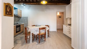 A dining area with a table and chairs, a kitchen in the background, wooden beams on the ceiling, and a white radiator. - Apartment 'La Porta Del Palio' with Private Terrace, Wi-Fi and Air Conditioning (Siena)