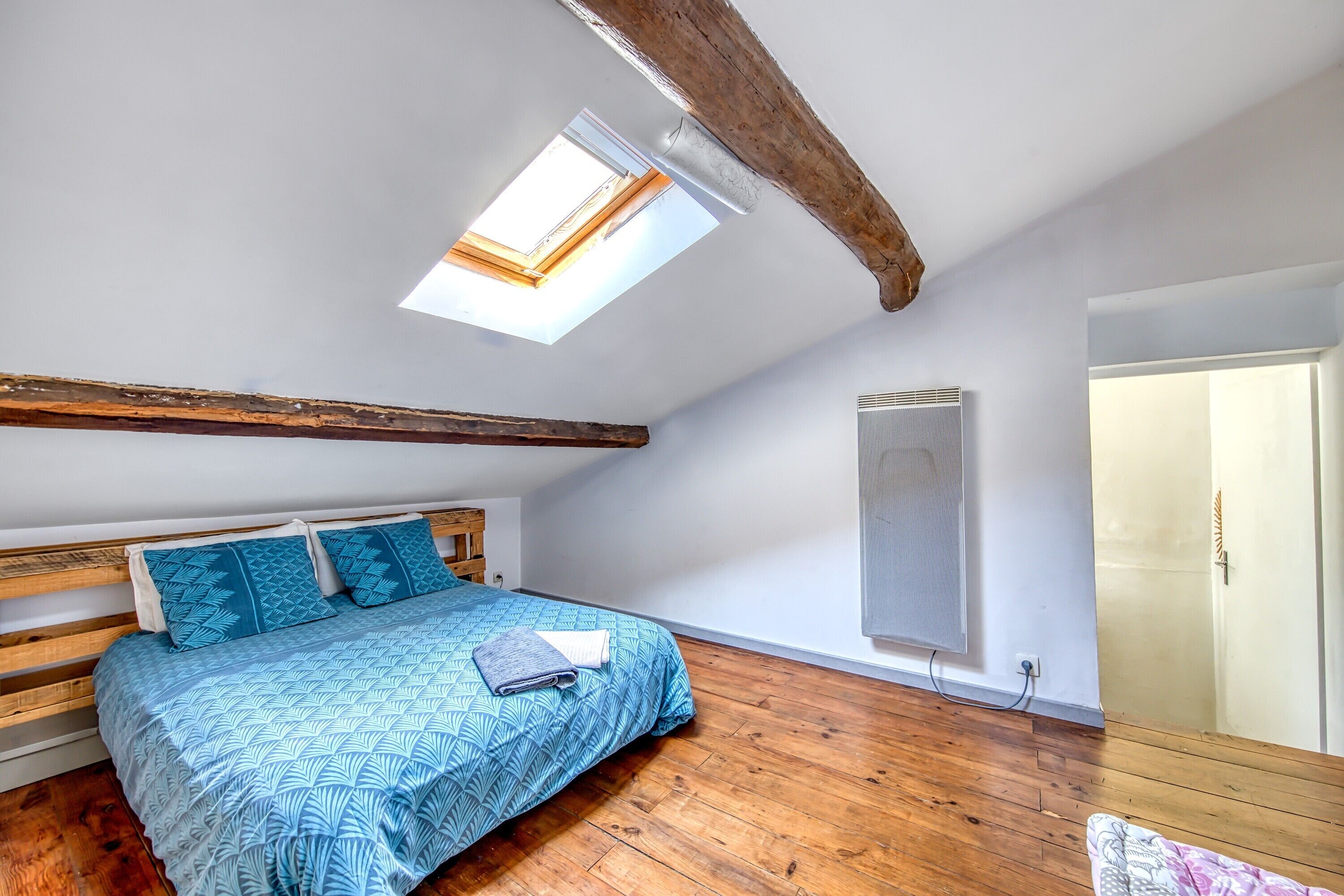 A bedroom with a sloped ceiling, a skylight, a bed with patterned bedding, a wooden headboard, and a radiator.