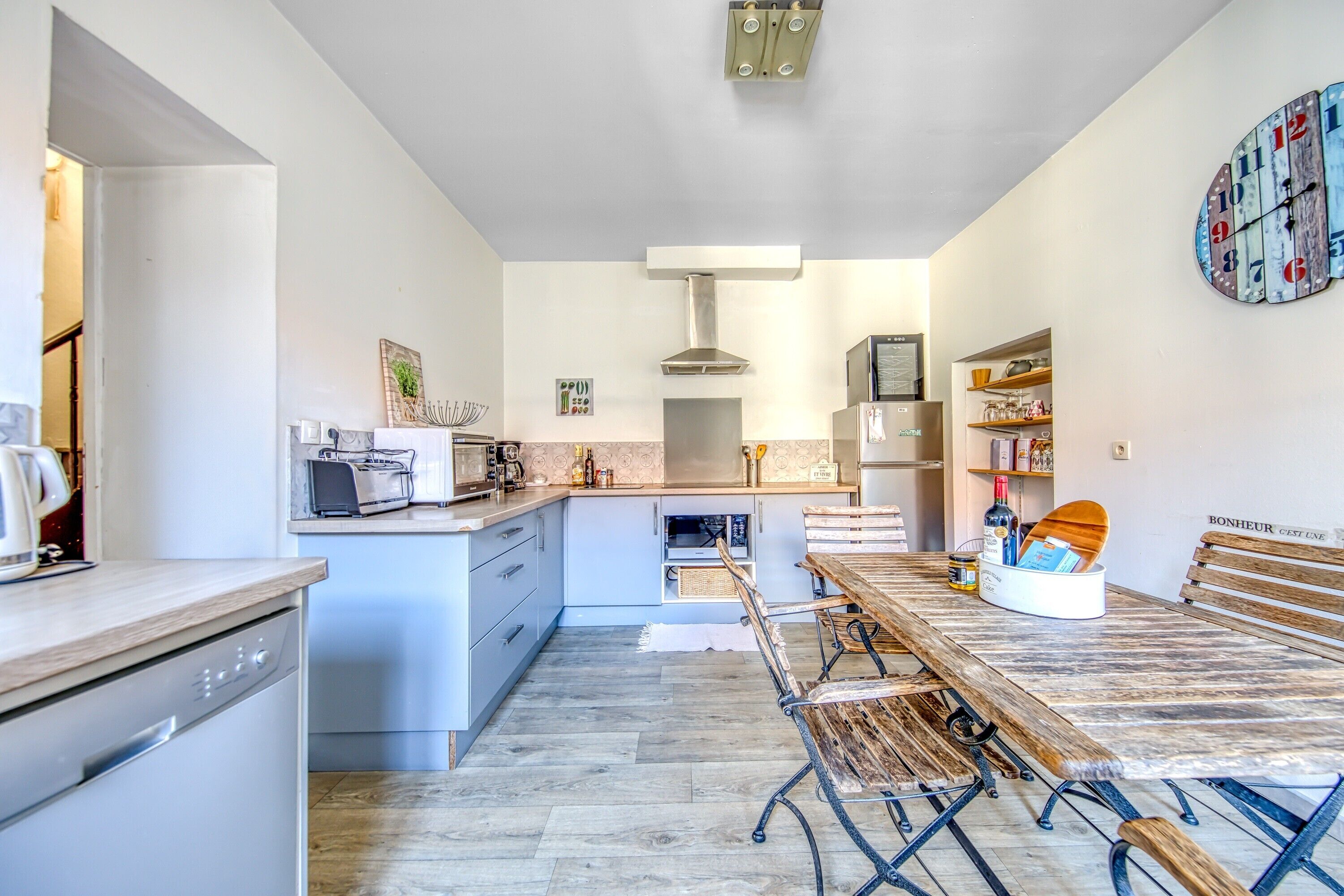 Een moderne keuken met een centraal eiland, inbouwapparatuur en een eetgedeelte met een houten tafel en bankjes.
