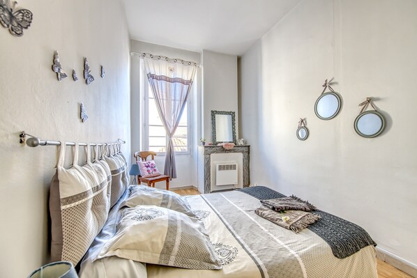 Un dormitorio con cama, una silla, chimenea y adornos en la pared.