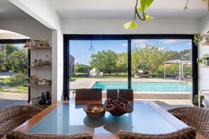 A modern room with a glass table, wicker chairs, a view of a swimming pool, and a bookshelf with various items. - Holiday Home 'Casa Chocolate' with Mountain Views, Private Pool and Wi-Fi (Porto)
