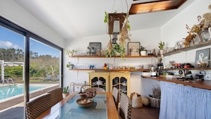 A modern kitchen with a glass-top dining table, built-in shelves, and a view of a swimming pool. - Holiday Home 'Casa Chocolate' with Mountain Views, Private Pool and Wi-Fi (Porto)