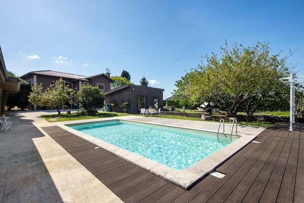 A rectangular swimming pool with a wooden deck surrounding it, a house in the background, and a tree to the right. - Holiday Home 'Casa Chocolate' with Mountain Views, Private Pool and Wi-Fi (Porto)