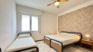A bedroom with two single beds, a ceiling fan, a window with curtains, and a stone-patterned wall.