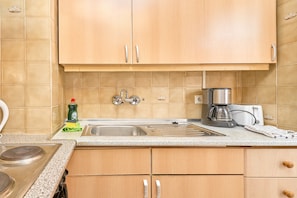 Una cocina con armarios de madera, un lavamanos de acero inoxidable, una cafetera y un hervidor.