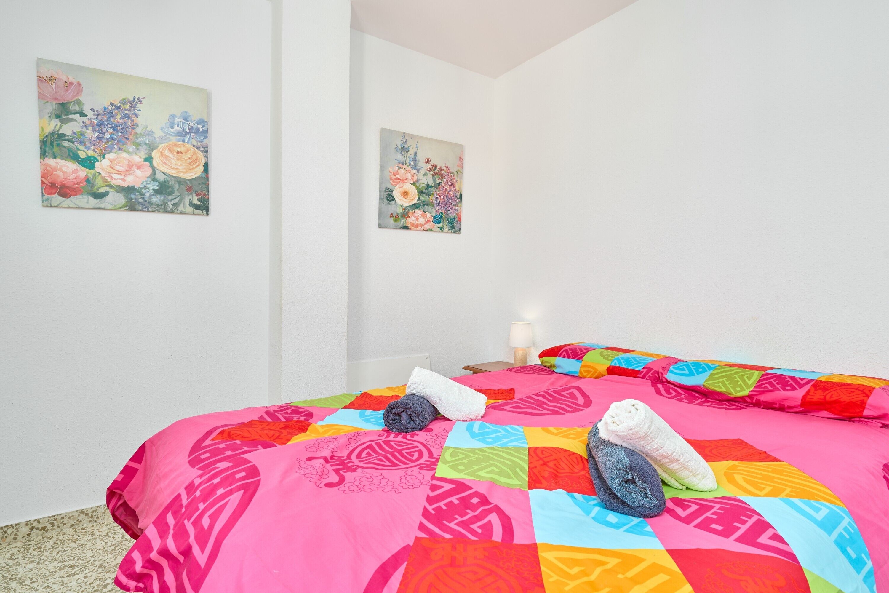Ein Zimmer mit zwei Betten, bunter Bettwäsche und zwei floralen Bildern an den Wänden.