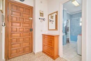 Eine Holztür, ein kleiner Holzschrank, ein Spiegel und ein Badezimmer mit Dusche und Waschmaschine.