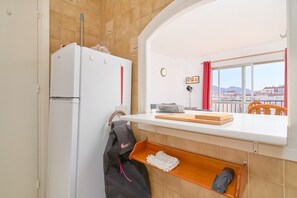 Eine Küche mit einem weißen Kühlschrank, einem Holzregal, einem Fenster mit Aussicht und einem roten Vorhang.