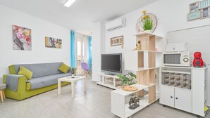 Uma sala de estar moderna com sofá, televisão, armários brancos e uma pequena mesa.