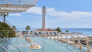 Vista para o mar com um farol, área de piscina e um edifício com telhado vermelho.