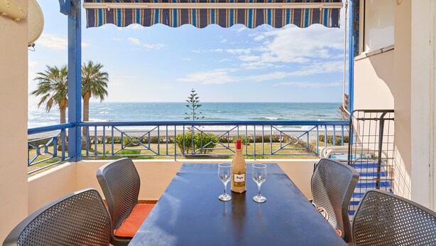 A balcony with a table, two chairs, a bottle of wine, and two glasses. The balcony overlooks the ocean and palm trees. - Apartment 'Jardines Del Mar' with Sea Views, Private Terrace and Wi-Fi (Torrox)