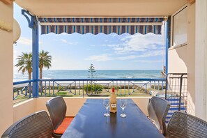 Een balkon met een tafel, twee stoelen, een fles wijn en twee glazen. Het balkon biedt uitzicht op de oceaan en palmbomen.