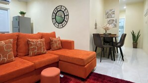Una sala de estar con un sofá modular, una mesa de comedor con sillas, una alfombra roja y un reloj de pared.