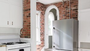 A kitchen with white cabinets, a gas stove, a stainless steel refrigerator, and a brick wall.