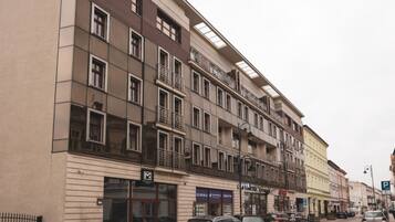 Un edificio de varios pisos con balcones, escaparates y coches aparcados en la planta baja.