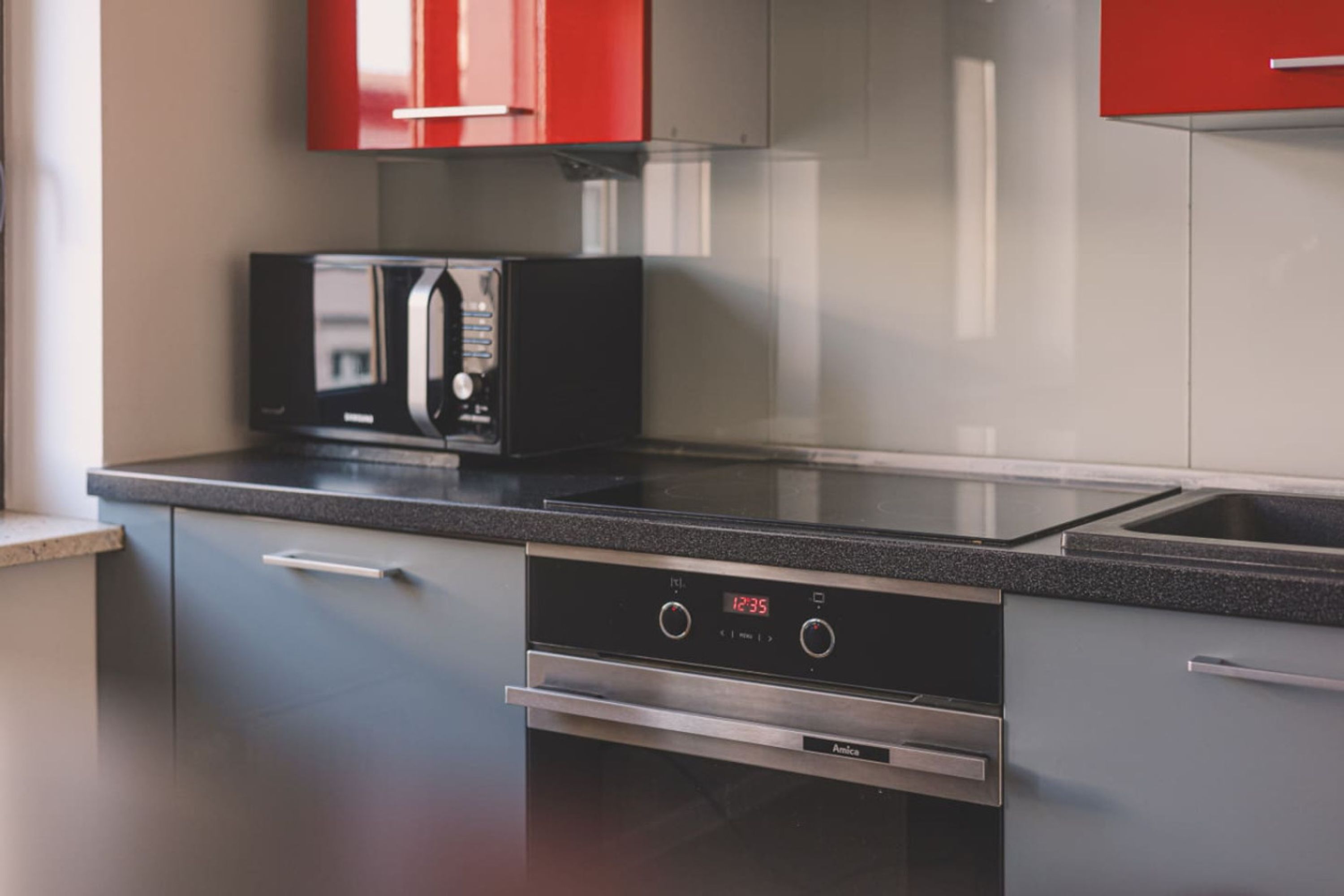 A modern kitchen with stainless steel appliances, including a microwave and oven, and red cabinets.
