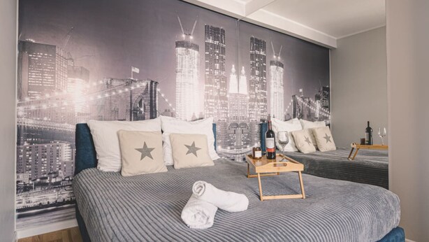 A hotel room with a large bed, a cityscape mural on the wall, a wooden nightstand, and a neatly made bed with a towel. - Dream 14 Przytulne Studio Centrum Bydgoszczy (Bydgoszcz)