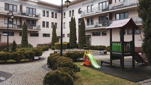 A courtyard with a playground, including a slide and a bench, surrounded by neatly trimmed bushes and trees. - Dream 14 Przytulne Studio Centrum Bydgoszczy (Bydgoszcz)