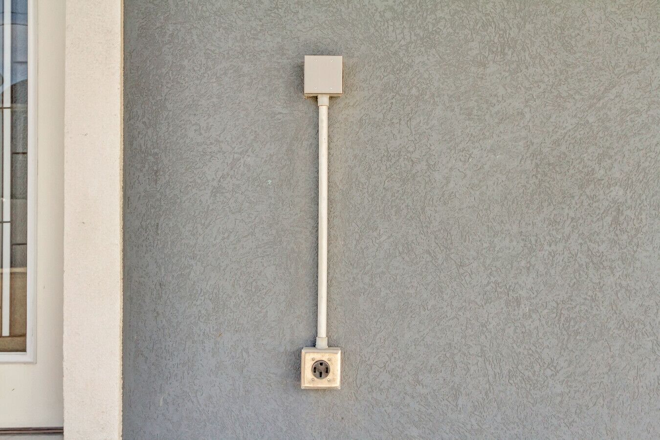 A wall-mounted electrical box with a cable on a textured grey wall.