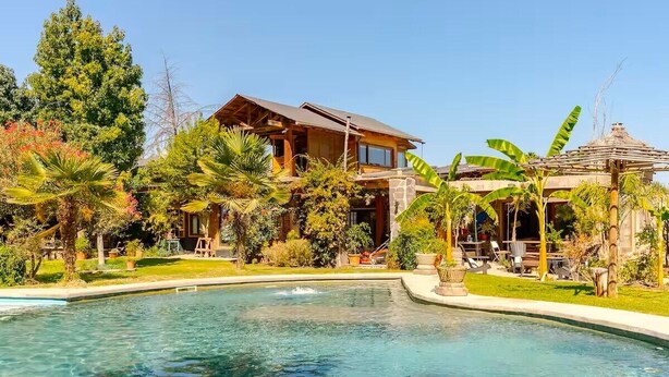 A pool area with a wooden house and tropical plants. - Wonderful large family cottage (Curacavi-Lolenco)