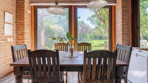 A dining area with a wooden table and chairs, large windows with a view of greenery, and hanging pendant lights. - Wonderful large family cottage (Curacavi-Lolenco)