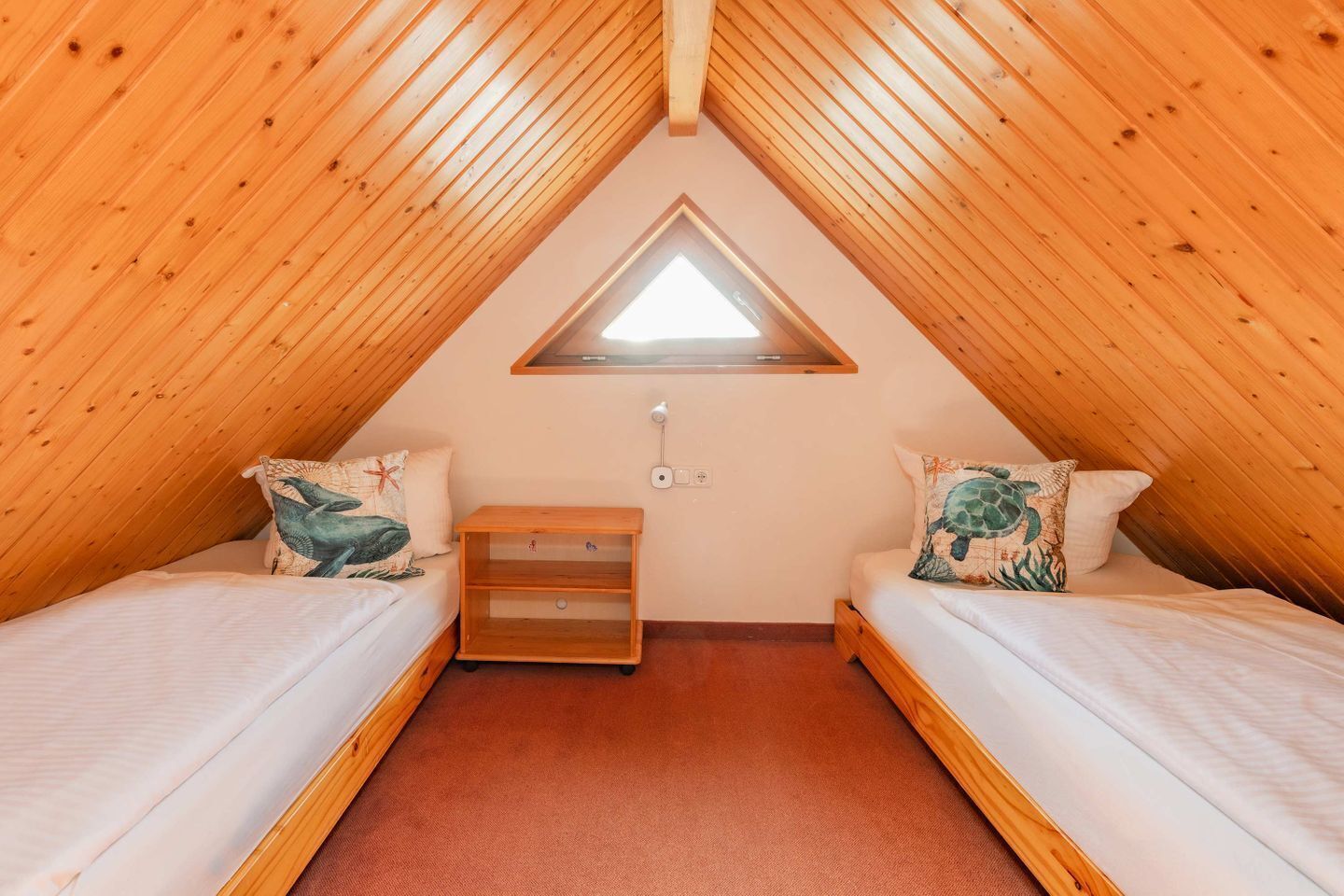 Ein kleines, dreieckiges Schlafzimmer im Dachgeschoss mit zwei Betten, einem Fenster und einem Nachttisch.