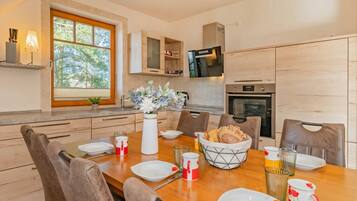 Une cuisine moderne avec des meubles en bois, une table à manger pour quatre personnes et une fenêtre donnant sur un paysage arboré.