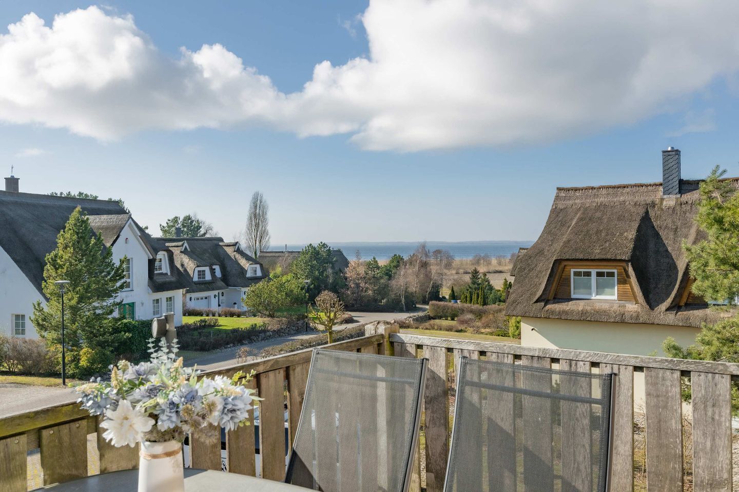 Un village côtier avec des maisons traditionnelles aux toits de chaume, une clôture en bois et une vue sur la mer.
