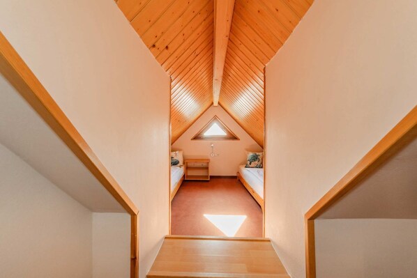 A narrow, wooden-framed attic bedroom with a sloped ceiling, a small window, and a single bed.
