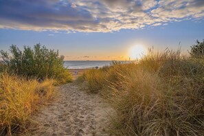 En sti af sand, der fører til en strand med udsigt over havet og en solnedgang.