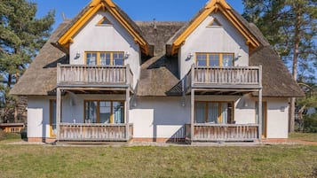 A two-story house with a thatched roof, wooden balconies, and a white exterior.