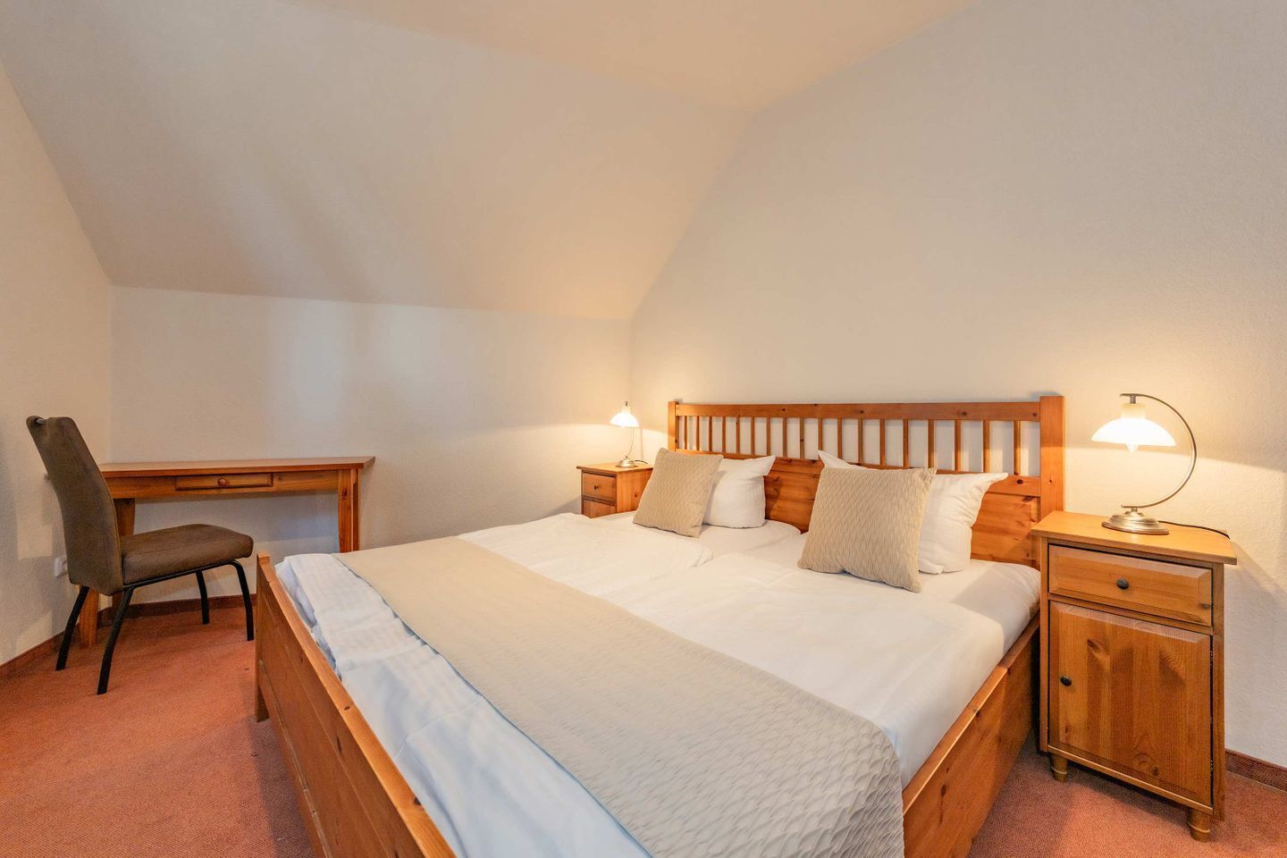 A bedroom with a bed, bedside tables, a desk, and a chair.