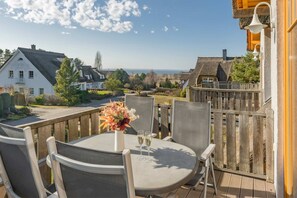 A balcony with a table, chairs, a vase with flowers, and a view of houses and the sea.