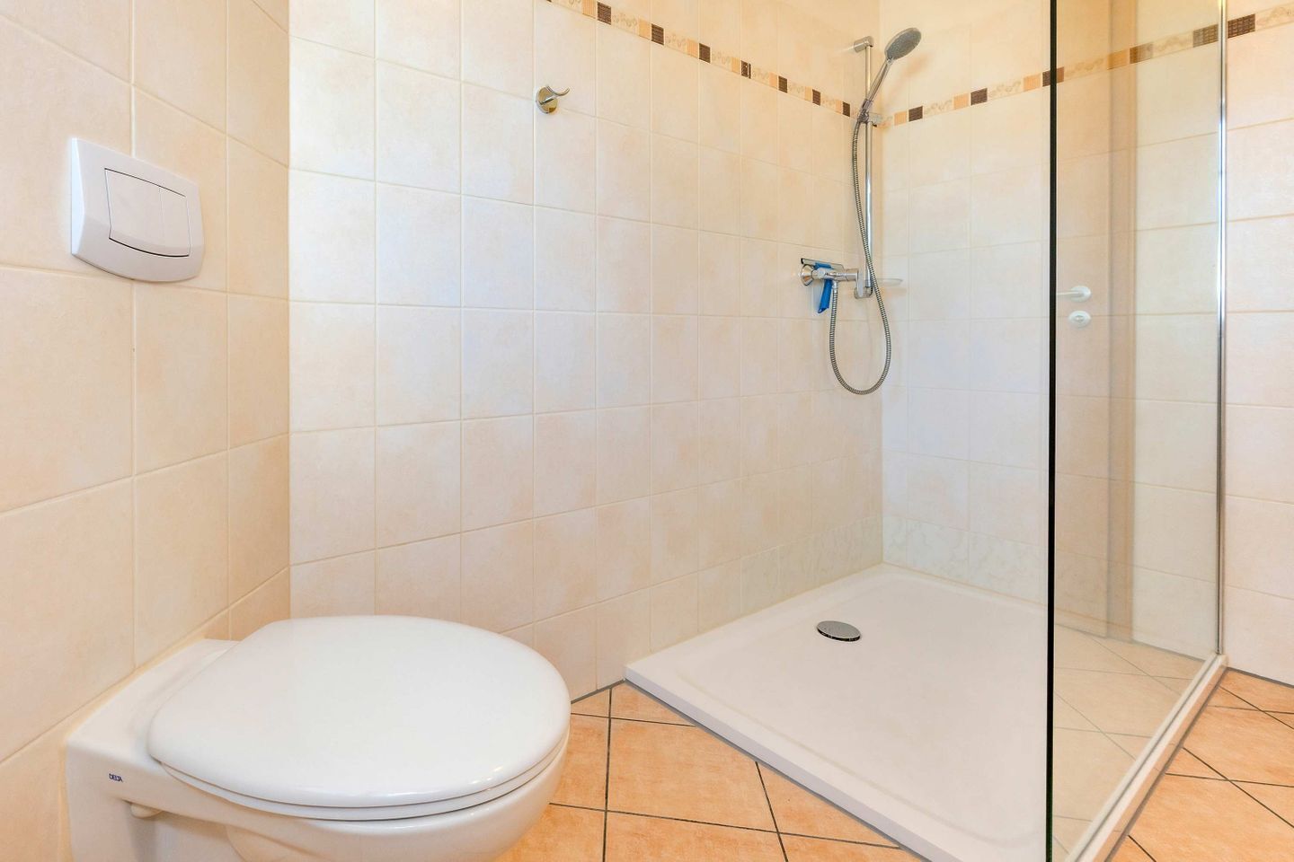 Un baño con inodoro, ducha con puerta de vidrio y suelo de baldosas.