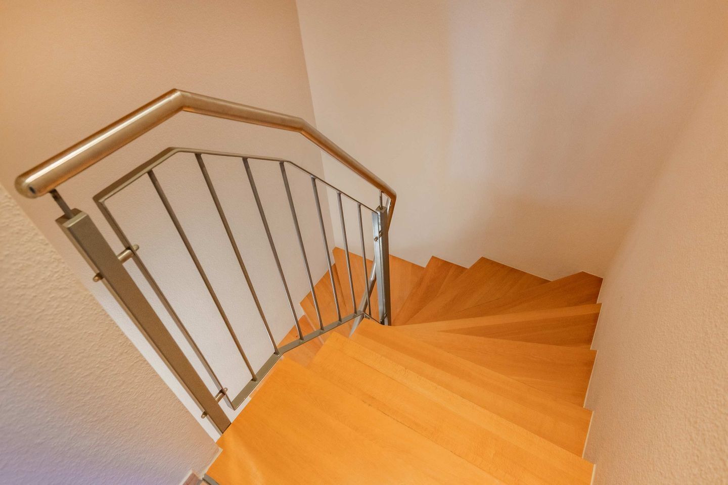 A wooden staircase with a metal handrail and a glass balustrade.