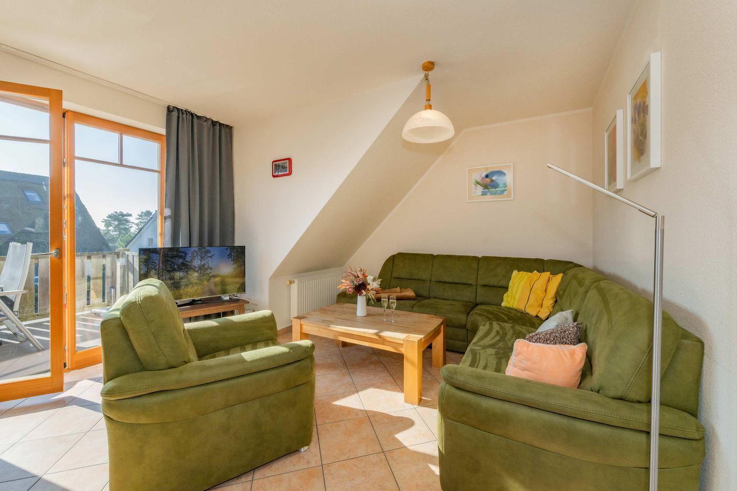 A living room with a green sofa, two green armchairs, a wooden coffee table, a TV, and a balcony with a view.