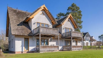 A two-story chalet with a thatched roof, wooden balconies, and a well-maintained lawn.