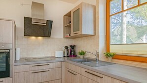 A modern kitchen with wooden cabinets, a built-in oven, a coffee maker, and a window with blinds.