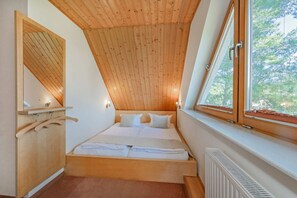 A bedroom with a sloped ceiling, a bed, a window, and a wooden wardrobe.