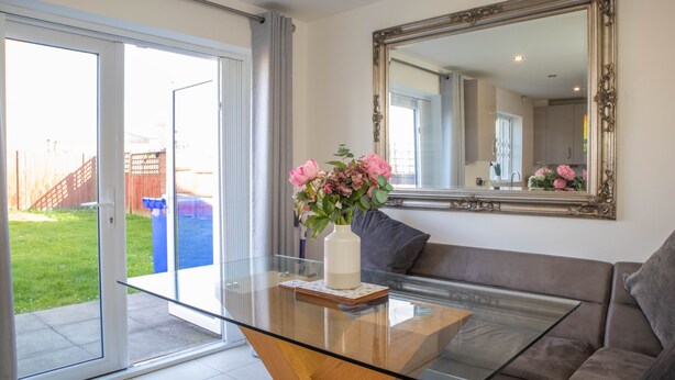 A living room with a glass coffee table, a vase with flowers, a large mirror, and a sliding glass door leading to a backyard.
