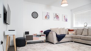 A modern living room with a flat-screen TV, a white cabinet, a sectional sofa, and a dartboard on the wall.