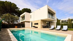 Una casa moderna de dos pisos con piscina, mobiliario exterior y fachada de piedra.