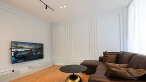 Una sala de estar moderna con un televisor de pantalla plana montado en la pared, una mesa de centro redonda con base metálica y un sofá de cuero marrón con cojines.