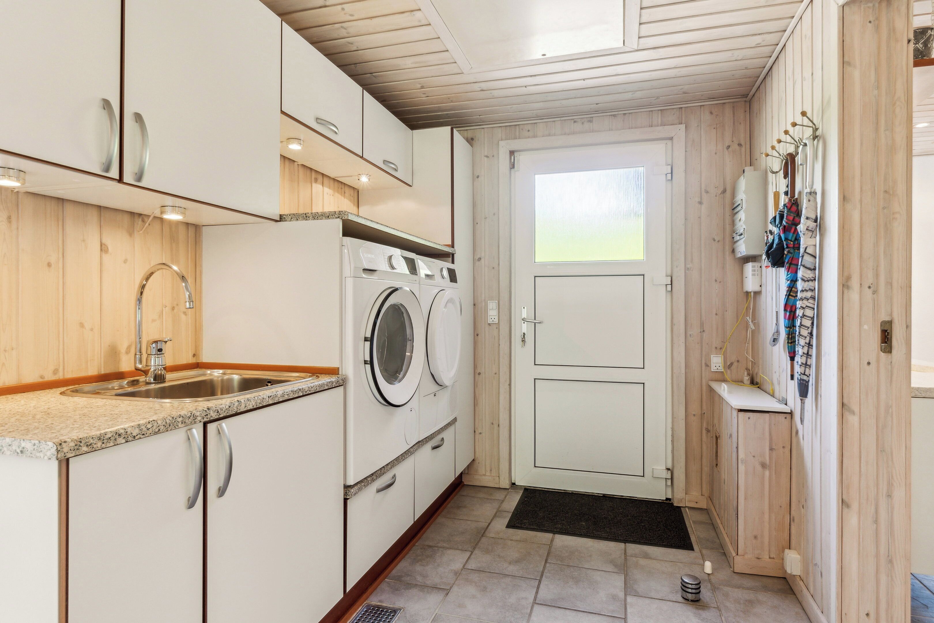 A compact kitchen with a sink, washing machine, and wooden cabinets.