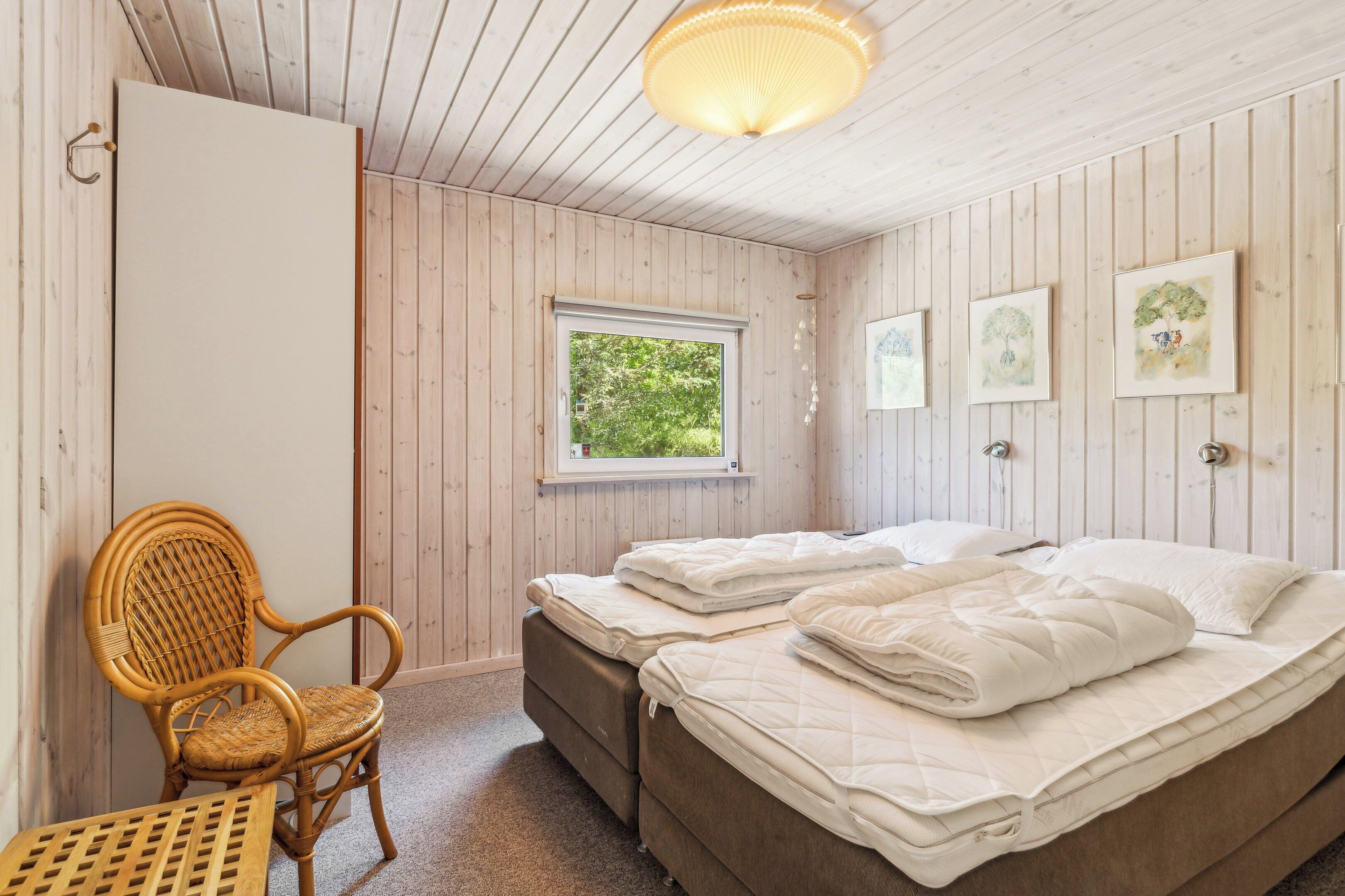 Et værelse med trævægge, et vindue, to senge, en stol og en hængende lampe.